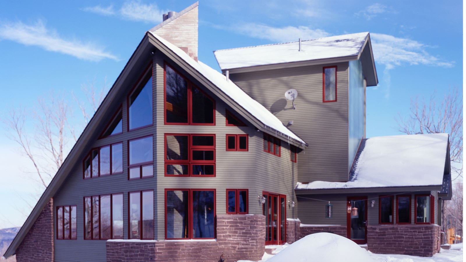 Front exterior view of The Avalanche, a modern ski home in Vermont. This home features a prow front, grey siding and brick accents.