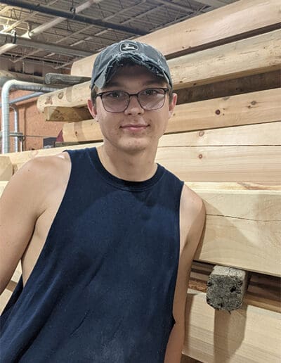 Man standing in front of stack of timbers.