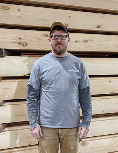 Man standing in front of stack of timbers.