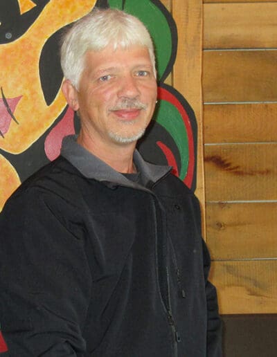 Man smiling at camera, standing in front of painting.