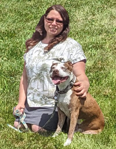 Woman sitting in field with smiling tan and white dog.