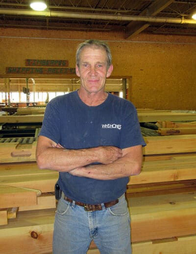 Man standing in River Road workshop in front of a bunch of timbers