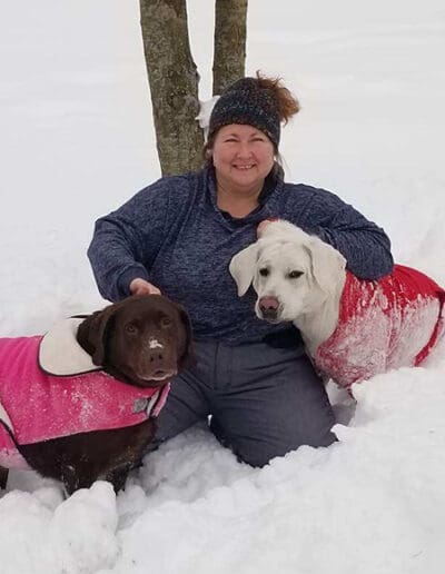 Woman sitting in snow with two dogs