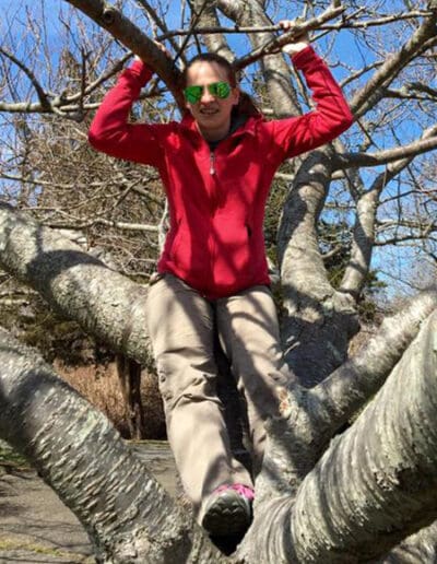 Woman sitting in tree with bare branches behind