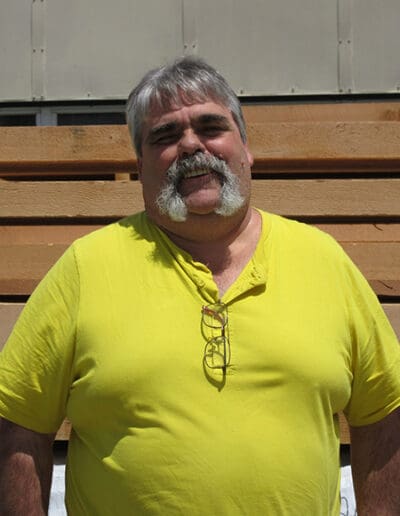 Man smiling in front of stack of timbers.