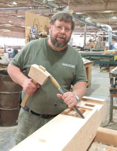 Man standing in workshop, holding mallet and chisel.