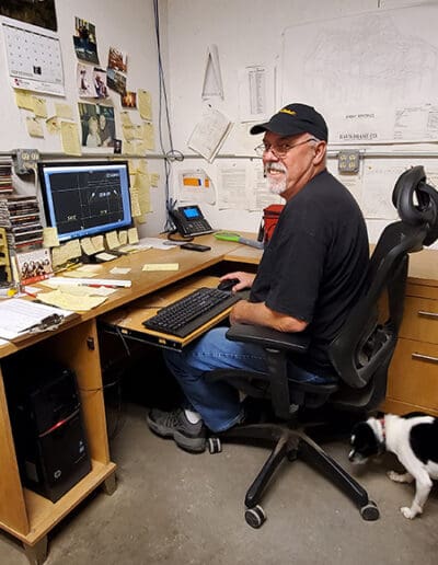 Man sitting at desk working on computer with blueprints behind him.